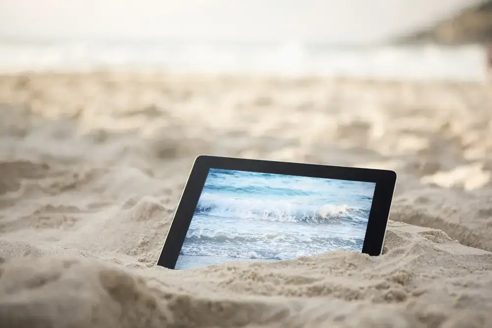 Tablet liegt im Sand, das Meer auf dem Bildschirm geht in die reale Brandung über – Symbol für den Website-Launch