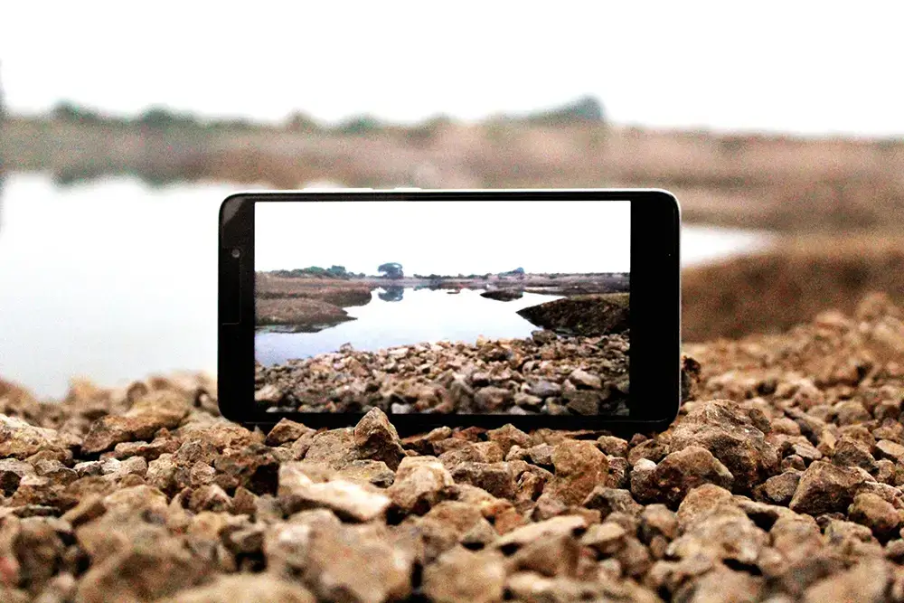 Smartphone liegt auf Kiesstrand, Bildschirm zeigt Wellen – Symbol für kleine Hürden und natürliche Bewegung im Website-Projekt